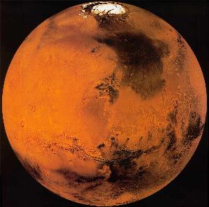Planet Mars, with a reddish surface interrupted by large dark patches and by bright white patches at the pole.
