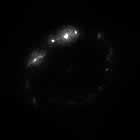 Black and white spiral galaxy image at violet   wavelengths, showing bright patchy light along the outskirts of a single spiral arm.