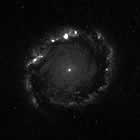 Black and white spiral galaxy image at blue     wavelengths, showing bright patchy light along the outskirts of spiral arms.