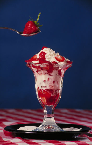 An ice cream sundae, topped with whipped cream and a strawberry.