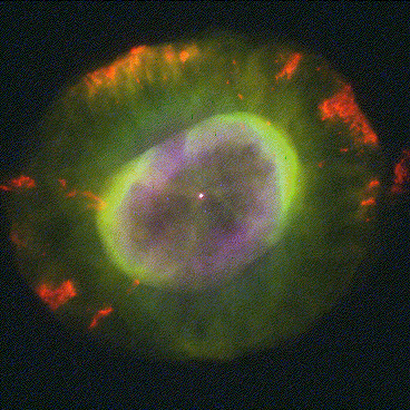 The central white dwarf is a tiny red-white dot, surrounded by glorious arcs and sheets of gas in green, red, and purple shades of light. The overall appearance is rather like an iridescent gem.
