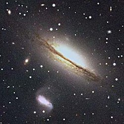 Telescope image of elliptical galaxy NGC 5078, a yellow oval with evidence of a band of dust.