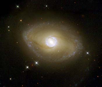 Image of NGC 6782, an inclined buttery yellow disk with bluer star-forming regions along the outer disk, and a bright white ring of light surrounding the central bulge.