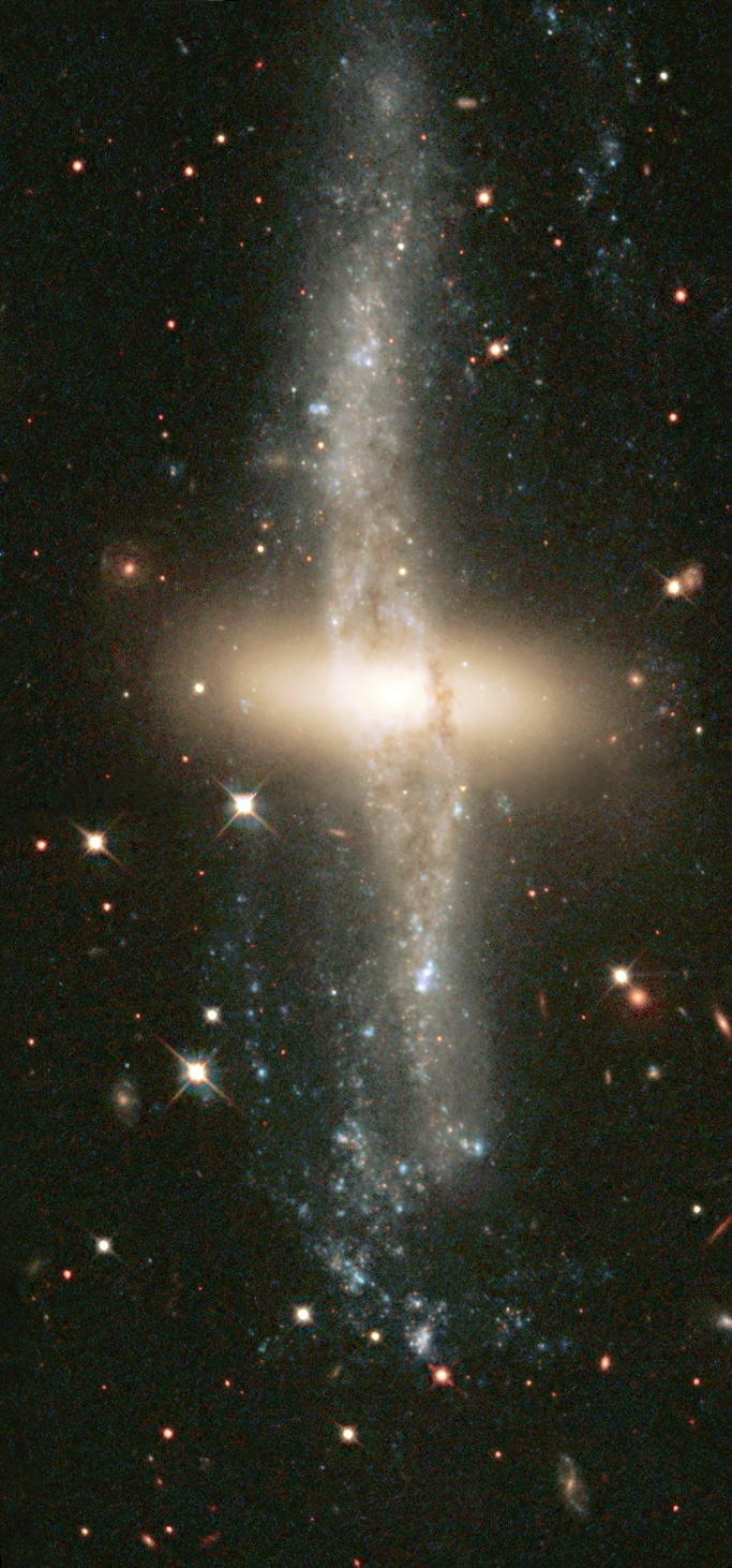 Image of NGC 4650A, showing a rare polar ring galaxy with an inner disk of older, reddish stars and a perpendicular larger ring of diffuse dust, gas, and stars. This is suspected to be the remnant of a galaxy-galaxy collision.