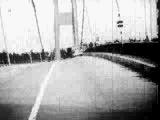 The Tacoma Narrows Bridge exhibiting unusual behavior, the metal and concrete structure banding and flexing from side to side quickly (in a fraction of a second) as a car on the bridge is raised and lowered quickly in height. The bulk of the flexing is shown occurring across the bridge, though there is also flexure along the long axis of the bridge running from one side of the water to the other.
