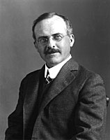 Photograph of Heber Curtis, shown seated while wearing a suit and tie and glasses.