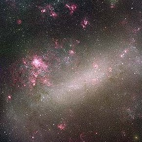 Telescope image of the Large Magellanic Cloud, showing bright disordered patches of white and violet light embedded in a diffuse cloud of white light.