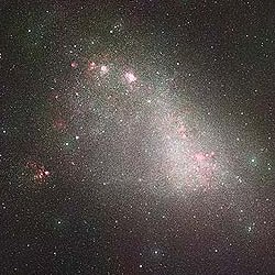 Telescope image of the Small Magellanic Cloud, showing disordered clumps of white and violet light embedded in a diffuse faint cloud of white light.