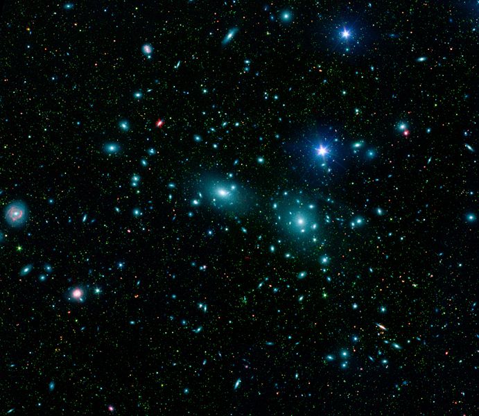 Telescope image showing thousands of galaxies gravitationally bound together into the Coma cluster. There are large elliptical galaxies and smaller spiral galaxies spinning wildly to form a shape not unlike a swarm of busy bees.