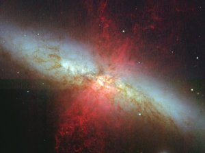 Telescope image of M82, showing disordered intersecting wings and spears of red, white, and dark yellow light.